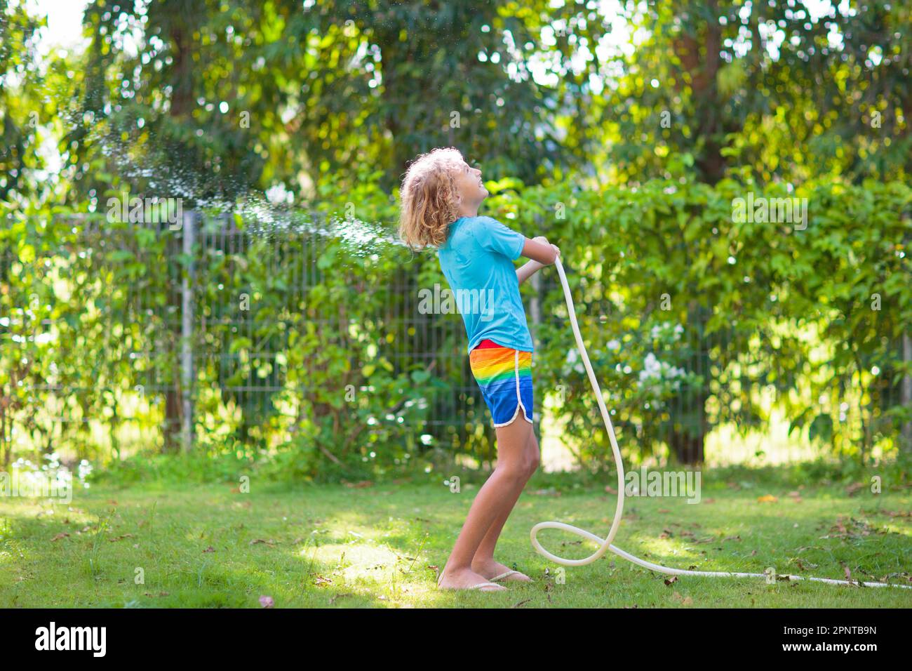 Kinder spielen mit einem Wasserschlauch. Sommergarten Outdoor Spaß für  Kinder. Ein Junge spritzt Wasser an einem heißen, sonnigen Tag. Kinder, die  Pflanzen im Garten bewässern Stockfotografie - Alamy