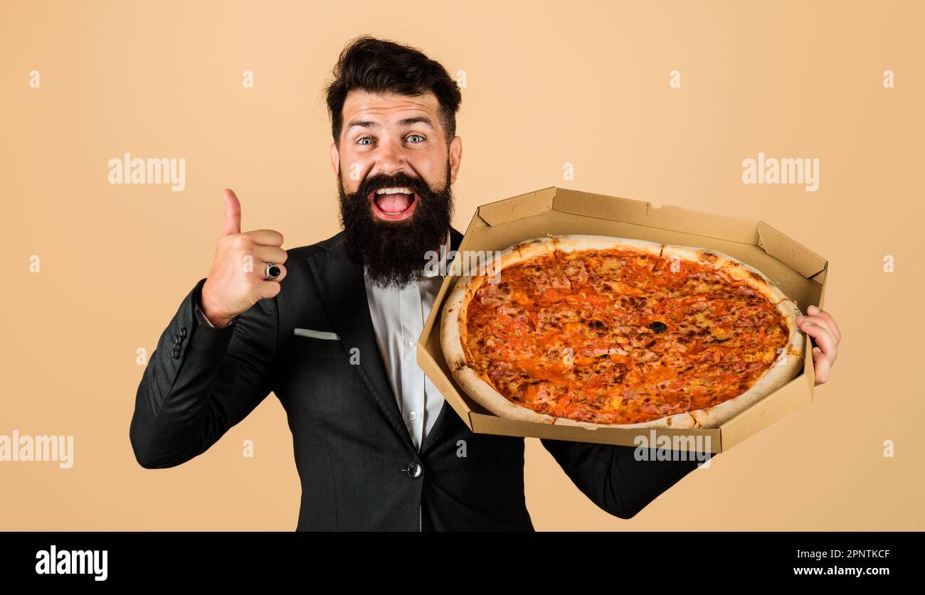 Ein bärtiger Mann mit Pizza, der Daumen nach oben zeigt. Probieren Sie köstliches Fast Food. Geschäftsmann mit leckerer italienischer Pizza. Bärtiger Mann im Anzug, der Pizza genießt. Pizza Stockfoto