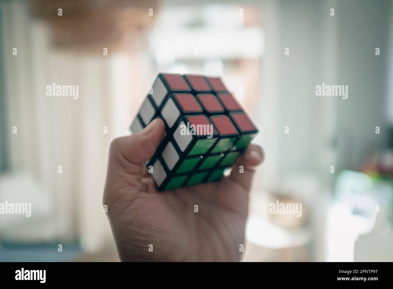 Die linke Hand hängt ein perfekt gefertigtes Rubik-Würfel-Puzzle in einem Haus Stockfoto