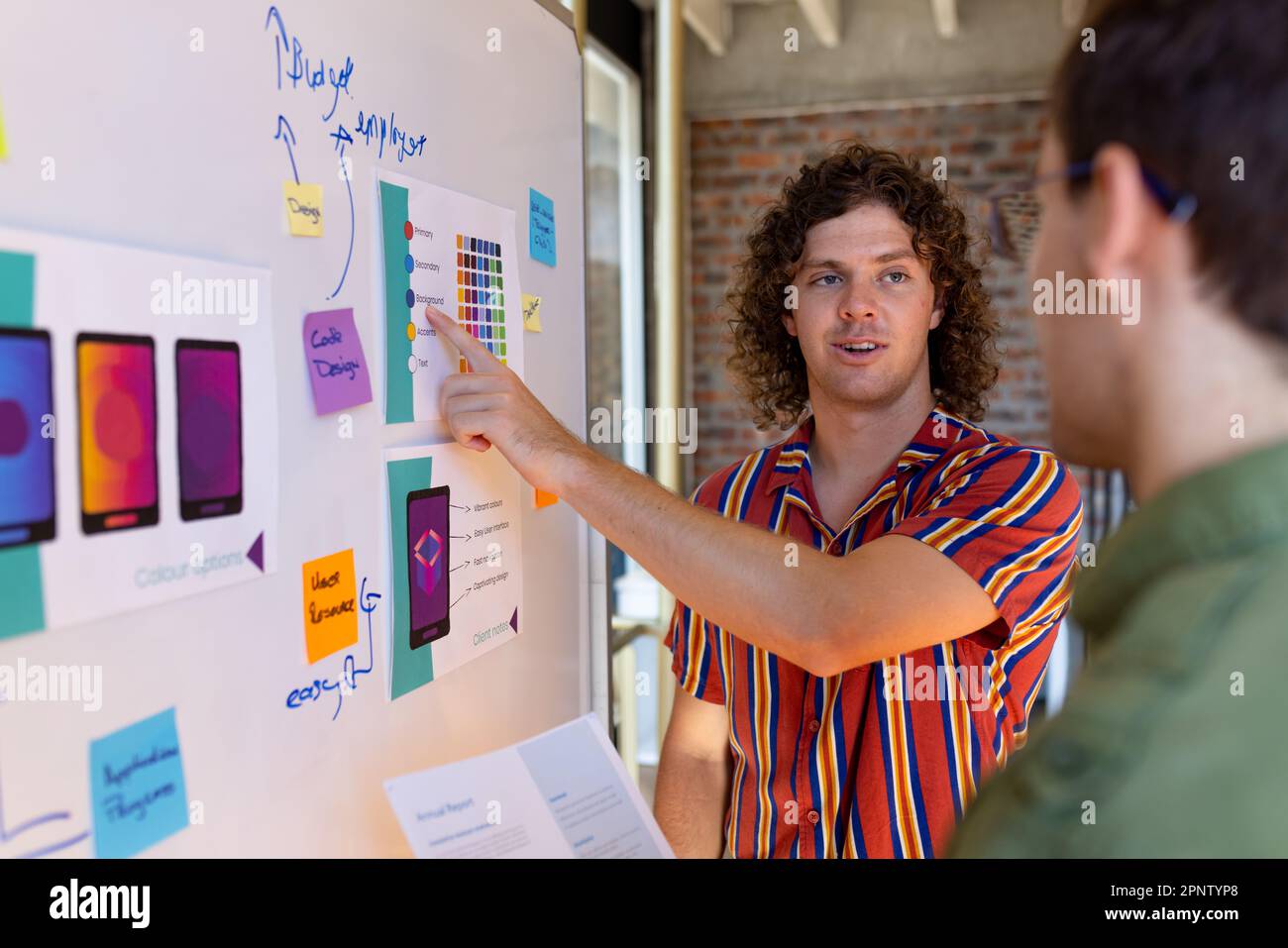 Zwei weiße männliche Designer schauen sich Konstruktionsmodelle an und diskutieren auf einem Whiteboard im Studio Stockfoto