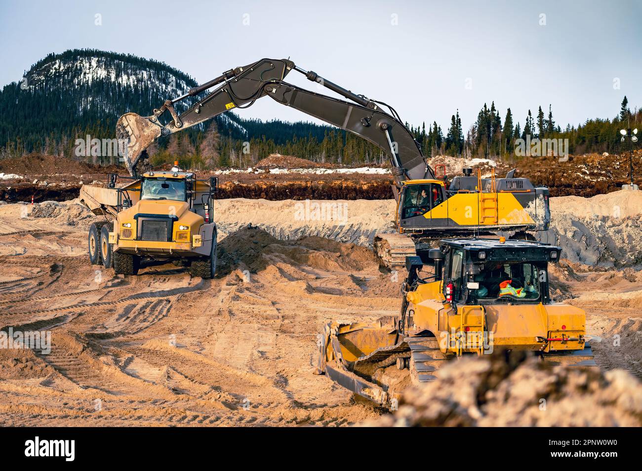 Bagger beladen einen Kipplaster mit Oberboden und einem sich nähernden Bulldozer Stockfoto