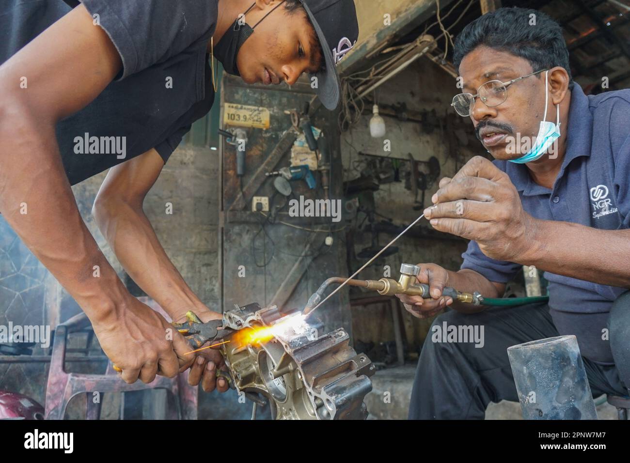 Mohan Jathusan, Left, und Radnasingam Mohan schweißen am 4. März 2022 in einer der wenigen Schweißwerkstätten in Mannar, Sri Lanka, einen Motorradmotor. (Vetrichelvi Chandrakala/Global Press Journal) Stockfoto