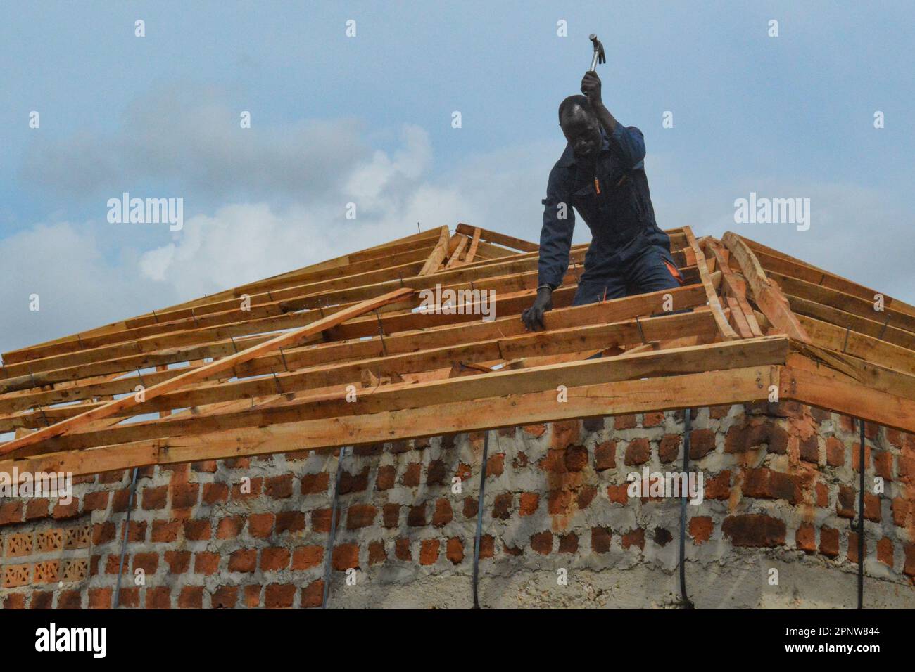 Scheich Gadafi Tumwebaze baut am 23. Juni 2022 ein Dach auf einem Haus in Kiwanga, Mukono, Uganda. Laut Tumwebaze gibt es in der Bauindustrie nicht viel Arbeit, da viele Projekte auf Eis gelegt haben, in der Hoffnung, dass die Materialpreise sinken. (Beatrice Lamwaka/Global Press Journal) Stockfoto
