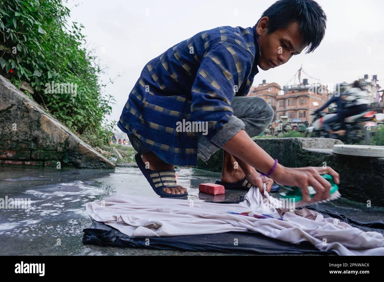 Bipul Limbu wäscht am 25. Oktober 2021 Kleidung in Sukedhara, Kathmandu, Nepal. Aufgrund eines Wassermangels kommen Limbu und seine Familie mindestens fünfmal am Tag hierher, um Wasser zu sammeln, Wäsche zu waschen und zu baden. (Shilu Manandhar/Global Press Journal) Stockfoto