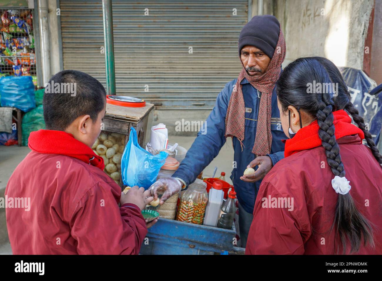 Jagar Nath Shah verkauft am 22. Dezember 2021 Pani puri, einen kugelförmigen Snack, an Schulkinder in Jana Marg, Kathmandu, Nepal. Shah, der Pani puri seit 15 Jahren in Kathmandu verkauft, musste während der Coronavirus-Pandemie vorübergehend seinen Betrieb schließen und in sein Dorf umziehen, um dort zu züchten. (Shilu Manandhar/Global Press Journal) Stockfoto