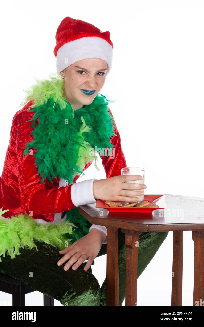 Nahaufnahme eines jungen Mädchens mit rotem weihnachtsmann-Hut wie grinch, das mit Milch in der Hand vor die Kamera niest, isoliert auf weißem Hintergrund. Lachend h Stockfoto