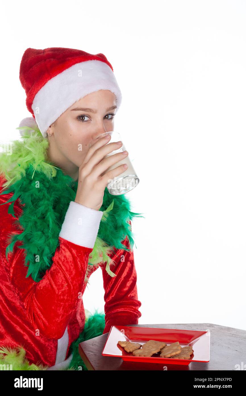 Nahaufnahme eines jungen Mädchens mit rotem weihnachtsmann-Hut wie grinch, der Milch trinkt, isoliert auf weißem Hintergrund. Menschliche Emotionen im Gesichtsausdruck Stockfoto