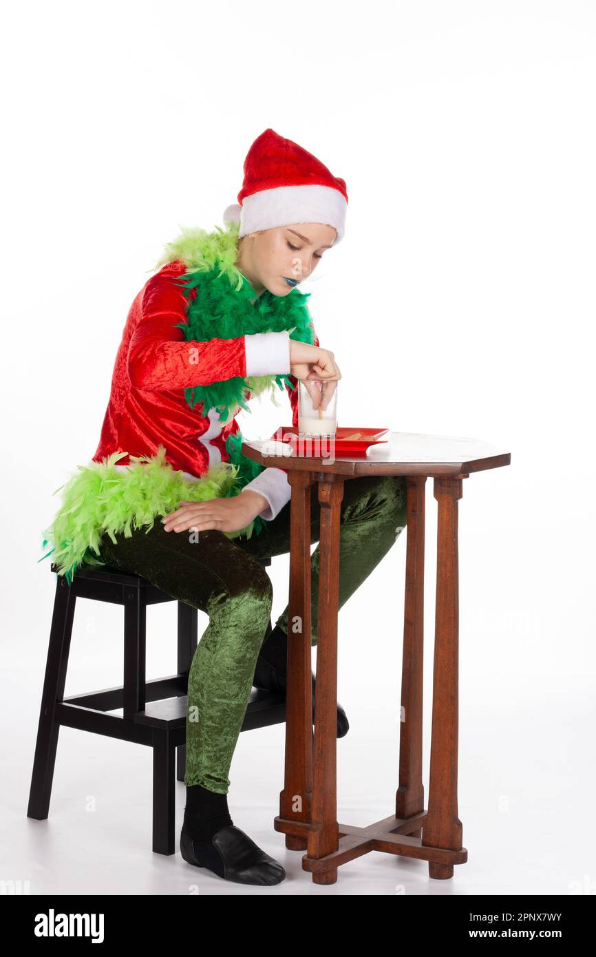 Vollbild eines jungen Mädchens mit rotem weihnachtsmann-Hut wie grinch Dipping Biscuit mit Konzentration, isoliert auf weißem Hintergrund. Menschliche Emotionen f Stockfoto