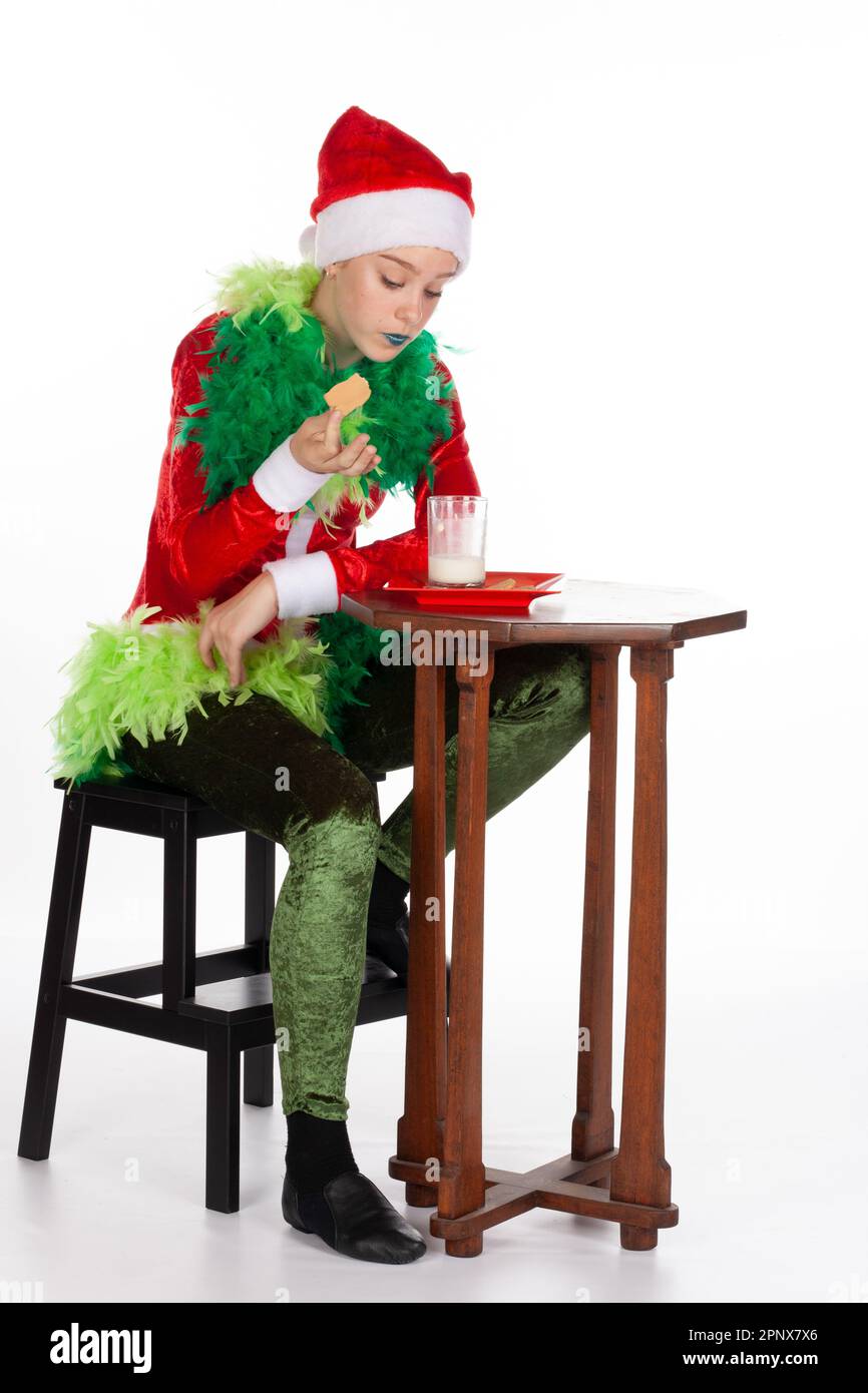 Vollbild eines jungen Mädchens mit rotem weihnachtsmann-Hut wie grinch Dipping Biscuit mit Konzentration, isoliert auf weißem Hintergrund. Menschliche Emotionen f Stockfoto