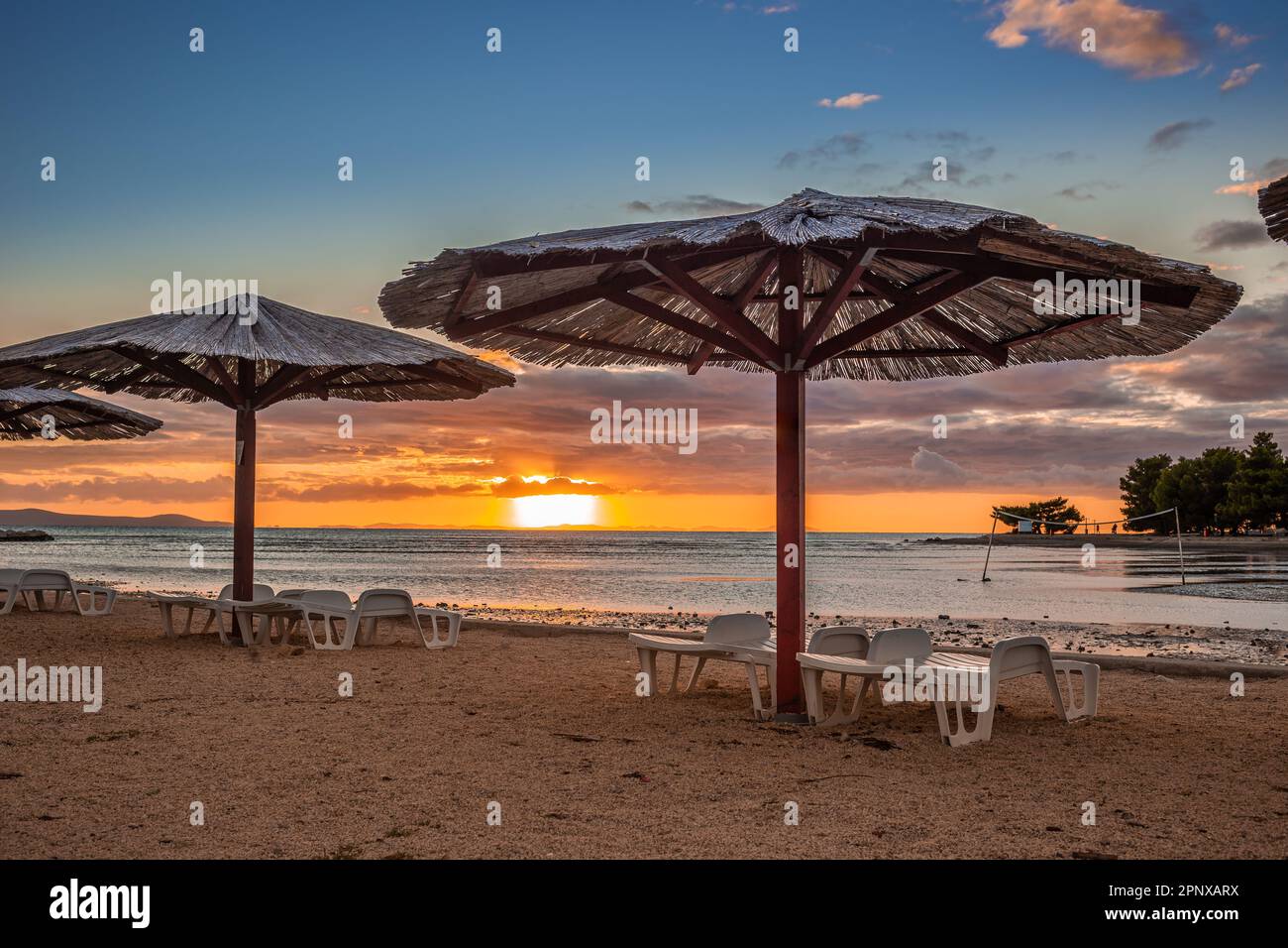 Zaton, Kroatien - Schilfschirme am leeren Strand von Zaton am Ende des Sommers mit dramatischen farbenfrohen Sonnenuntergängen im Hintergrund an der Adria Stockfoto