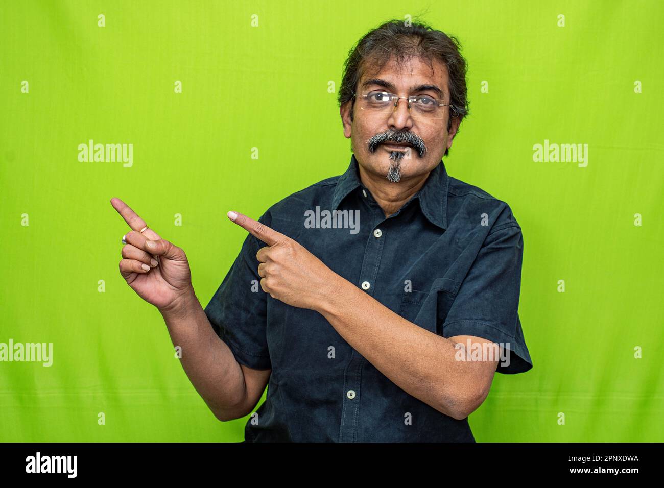 Der kluge Geschäftsmann in schwarzem Hemd und Brille zeigt mit beiden Zeigefingern die richtige Richtung an und steht vor einem grünen Hintergrund Stockfoto