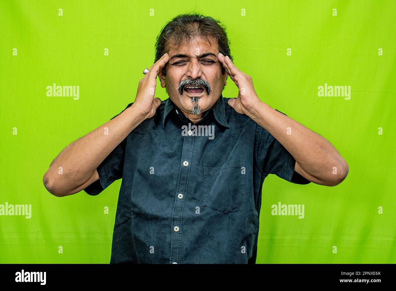 Der klug gekleidete Mann, der ein schwarzes Hemd trägt, scheint Migräne zu spüren, wenn er seine beiden Kopfseiten mit den Fingern seiner beiden Hände drückt Stockfoto