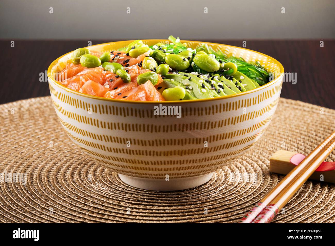 Appetitliche gesunde Schüssel mit Lachs und Gemüse serviert mit Sesamsamen und Essstäbchen auf dem Tisch Stockfoto