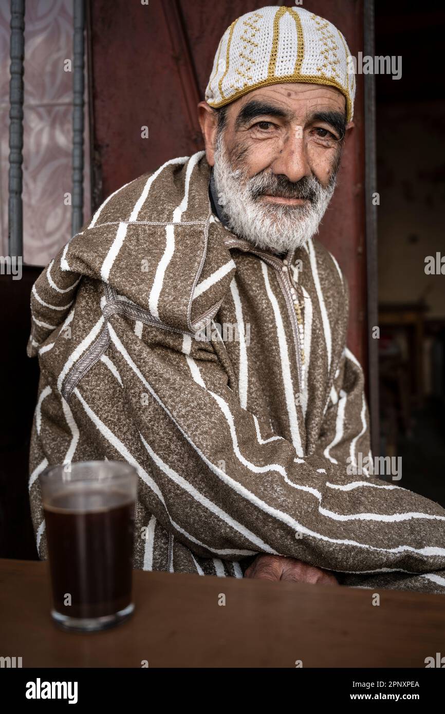 Porträt eines Mannes in einer Djellaba, der Tee vor der Tür einer kleinen Straßenbar trinkt. Stockfoto