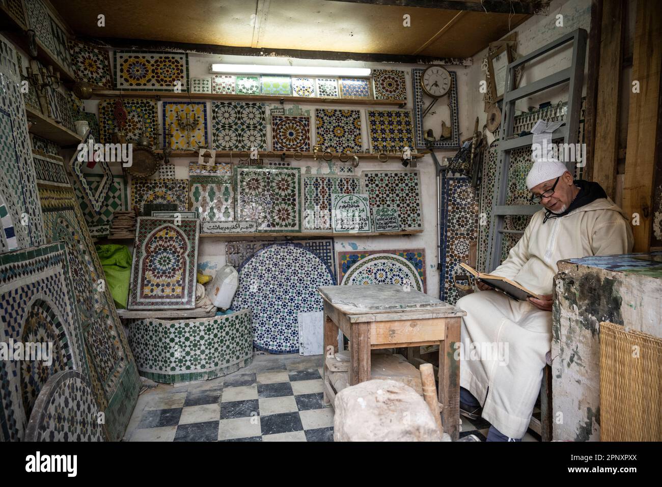 Ein Handwerker liest ein Buch, während er darauf wartet, dass ein Kunde in seinem Mosaikladen eintrifft. Stockfoto