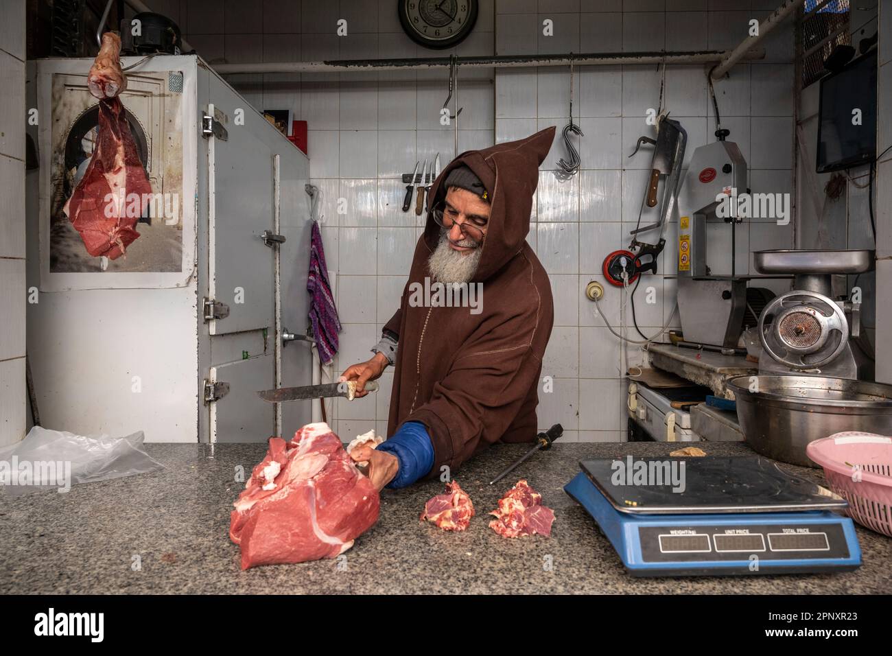 Metzger schneidet ein Stück Fleisch in seinem kleinen Laden in der Sefrou Medina. Stockfoto