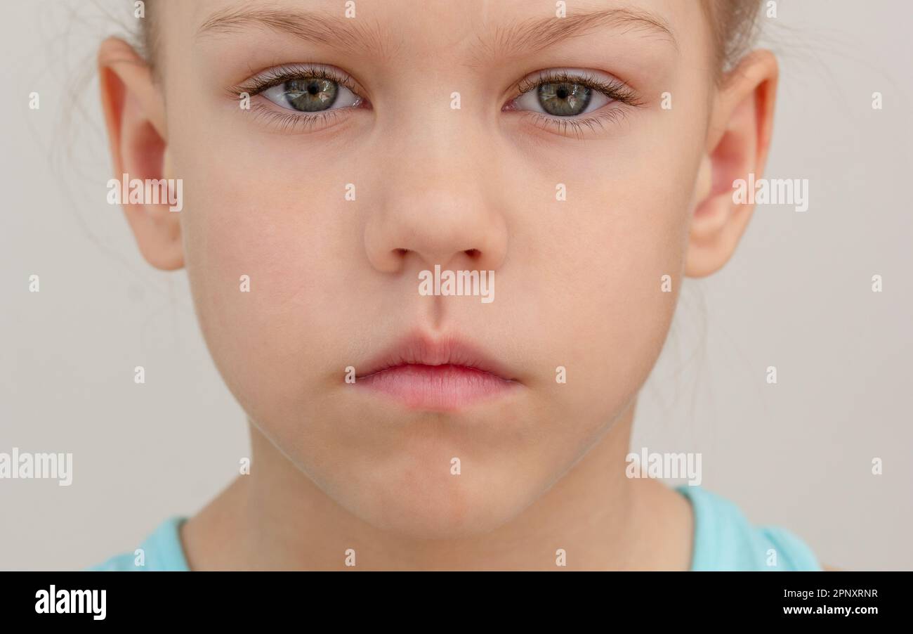 Ernstes Kindergesicht mit geschlossenen Lippen, gekürzter Kopf, kaukasisches kleines Mädchen von 6 7 Jahren auf grauem Hintergrund Stockfoto