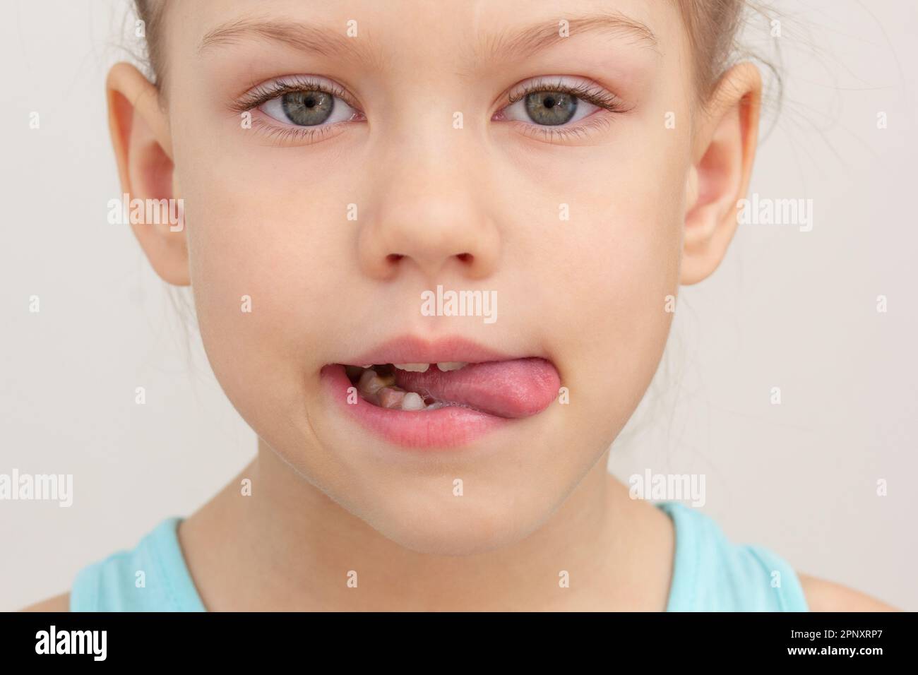 Kindsgesicht mit Zunge nach außen bis zur rechten Seite gekürzter Kopf Weißes Mädchen von 6 7 Jahren auf grauem Hintergrund Stockfoto