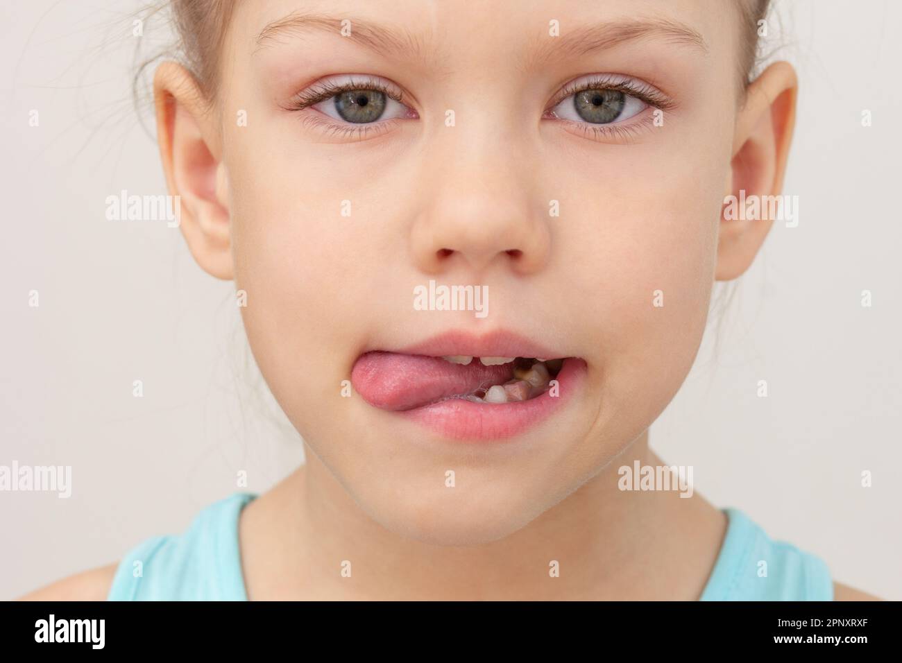 Kindergesicht mit Zunge nach außen nach links gekürzter Kopf Weißes Mädchen von 6 7 Jahren auf grauem Hintergrund Stockfoto