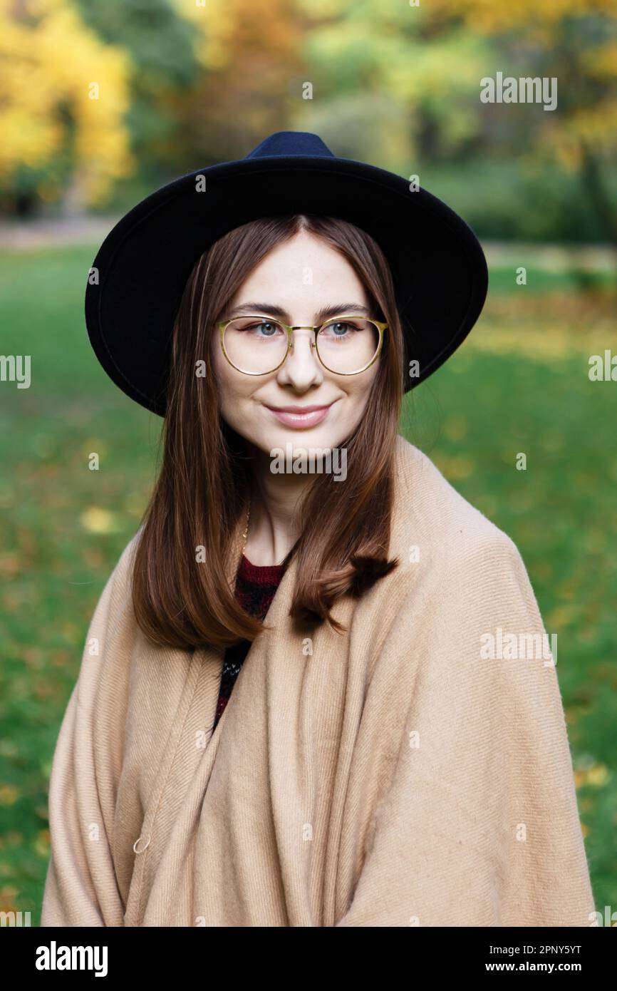 Braunhaarige Frau mit schwarzem Hut und Poncho geht im Herbstpark spazieren Stockfoto