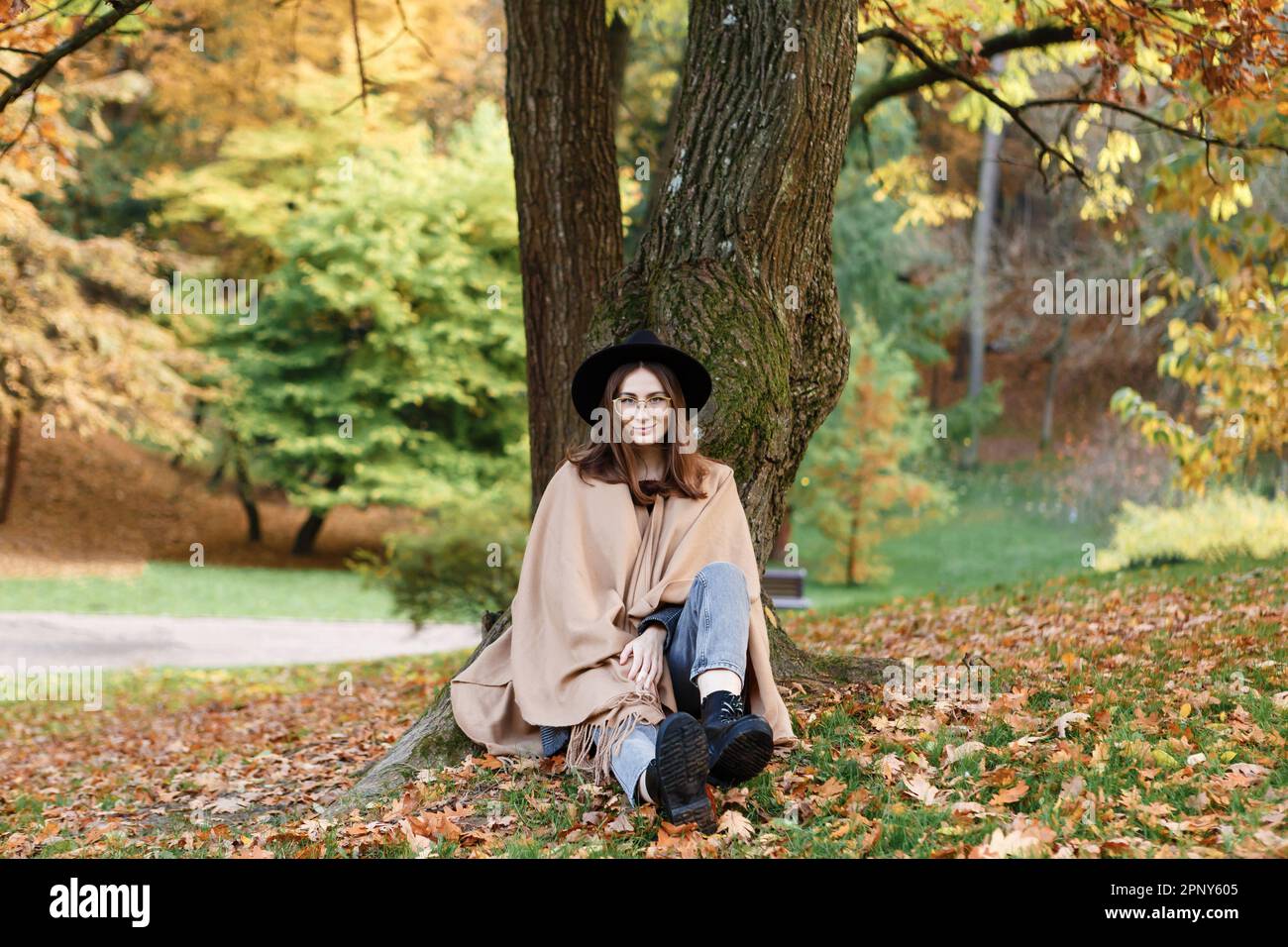 Braunhaarige Frau mit schwarzem Hut und Poncho im Park Stockfoto