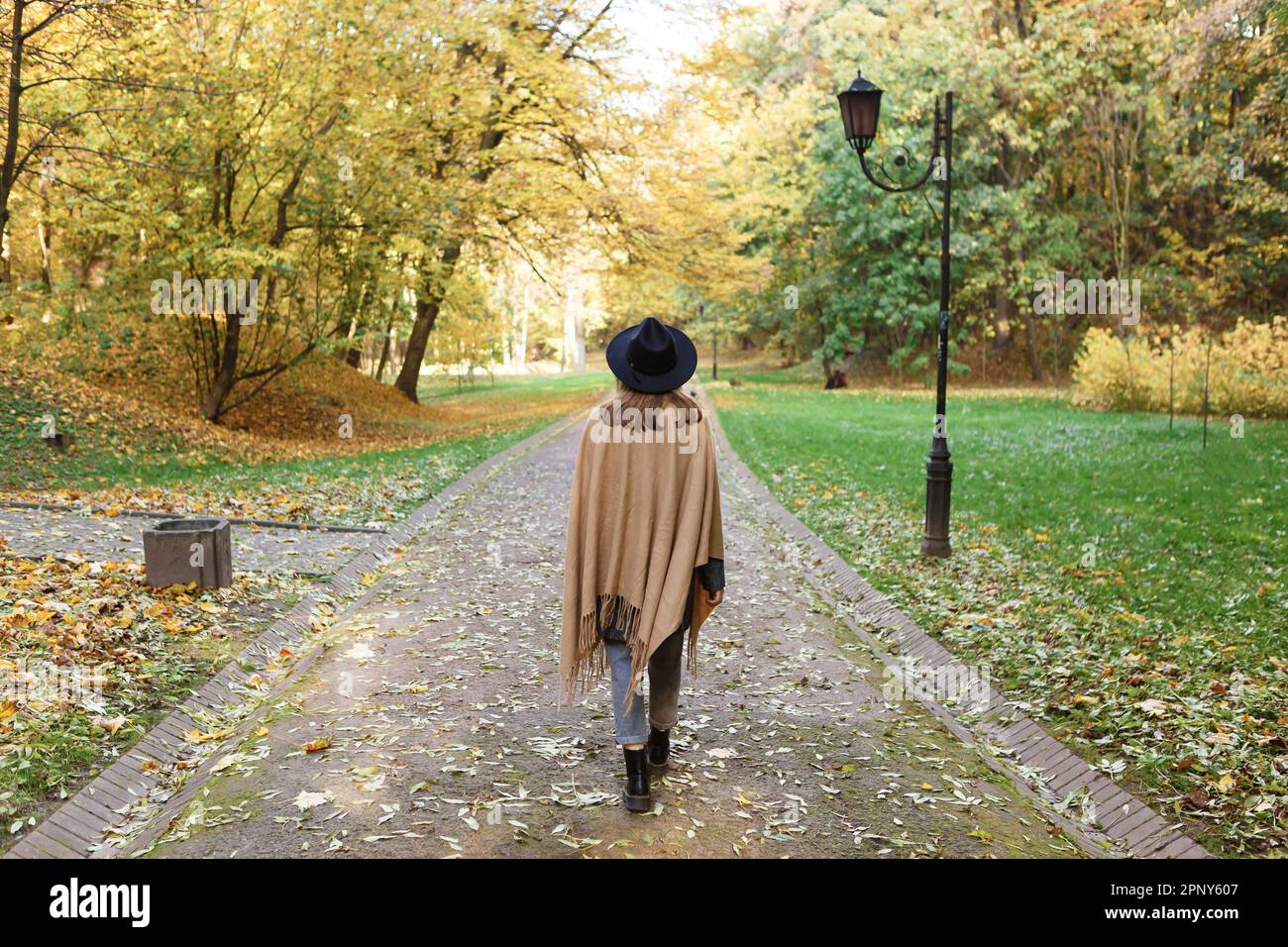 Braunhaarige Frau mit schwarzem Hut und Poncho geht im Herbstpark spazieren Stockfoto