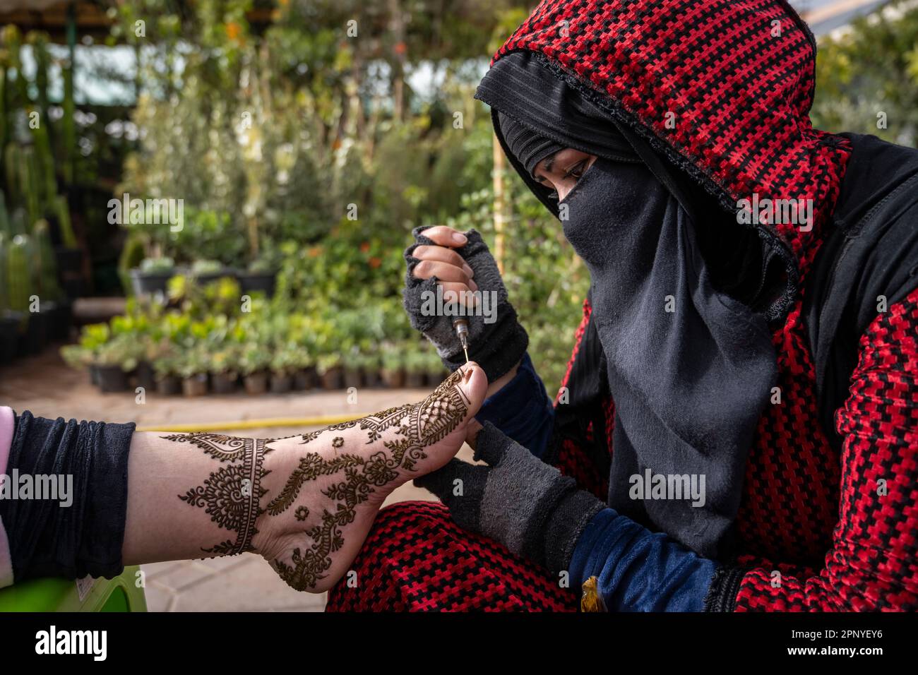 Muslimische Frau, die den Fuß eines Klienten mit Henna dekoriert, auf dem Platz Jemaa el-Fnaa in Marrakesch. Stockfoto