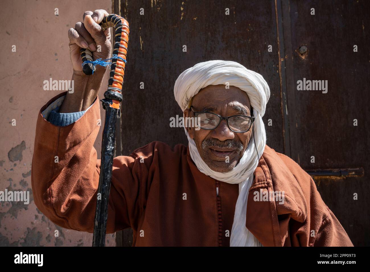 Porträt eines alten Mannes in traditioneller Kleidung, der sich an einen Stock lehnt. Stockfoto