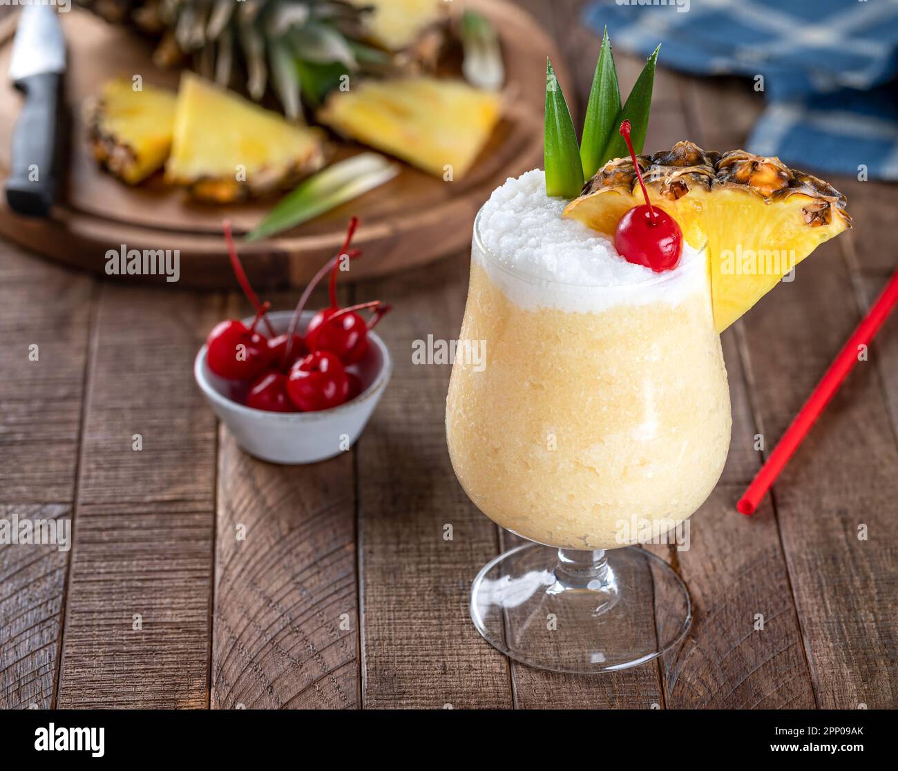 Pina-Colada-Cocktail mit Kirsche, Ananasscheiben und Blättern auf einem rustikalen Holztisch Stockfoto