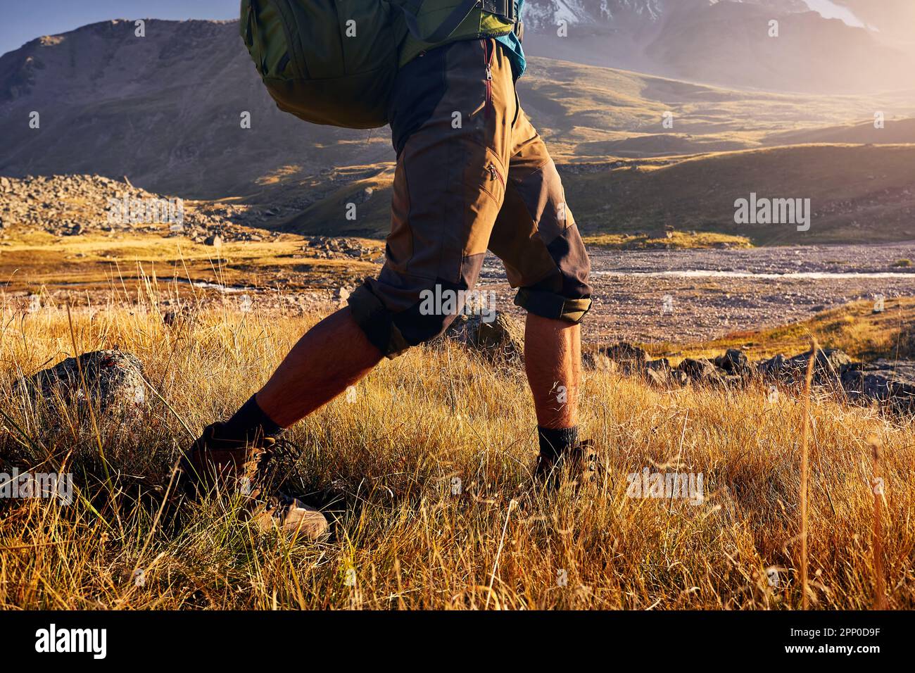 Ein Tourist mit Rucksack wandert im Herbst durch das Bergtal mit schneebedeckten Gipfeln in Almaty, Kasachstan. Beine mit Schuhdetails. Stockfoto