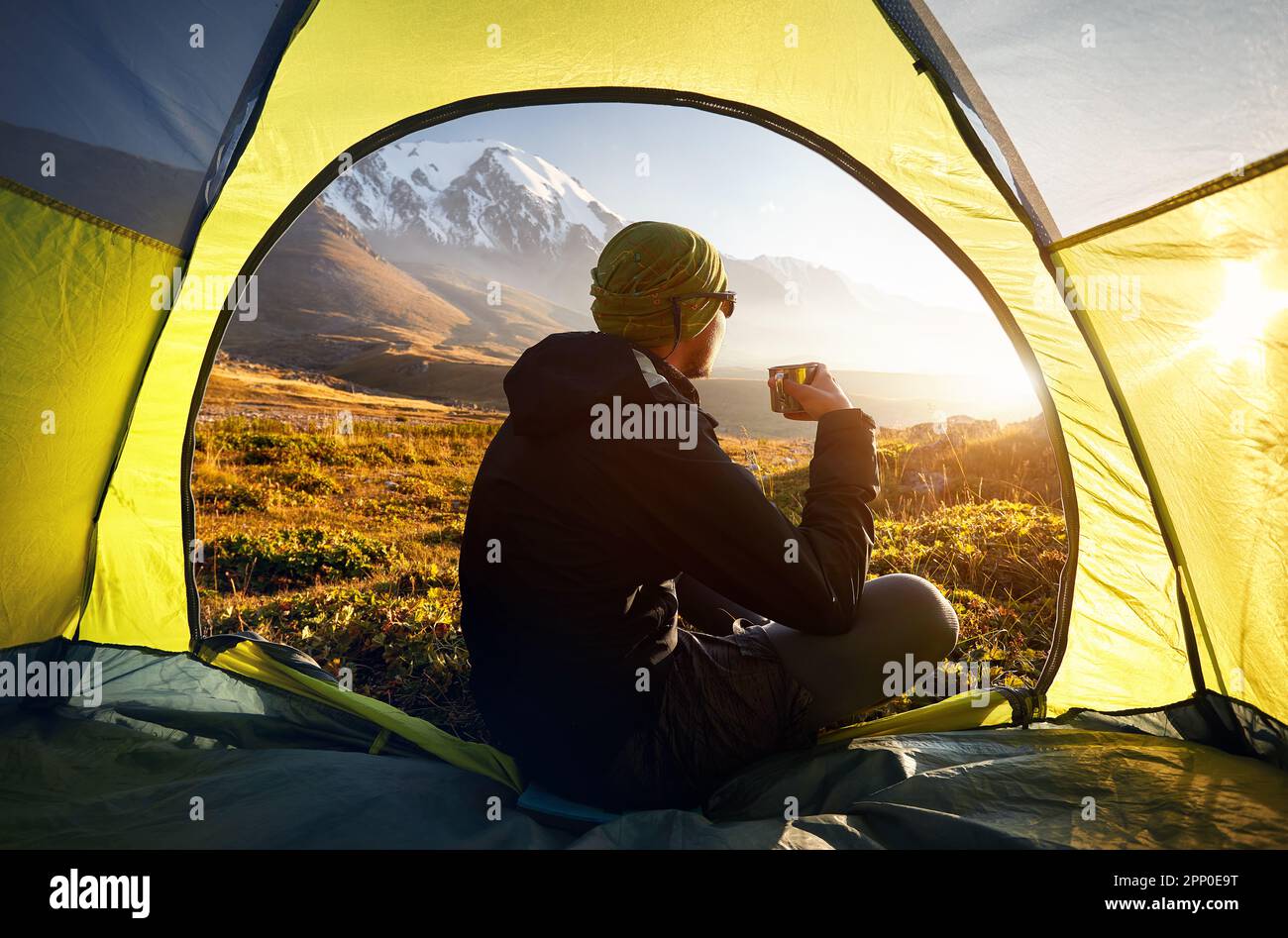 Blick aus einem Zelt mit Wanderer, heißem Tee und Blick auf das Gebirgstal mit Eisgletscherlandschaft bei Sonnenuntergang während der Wanderung in Zentral-Asi Stockfoto