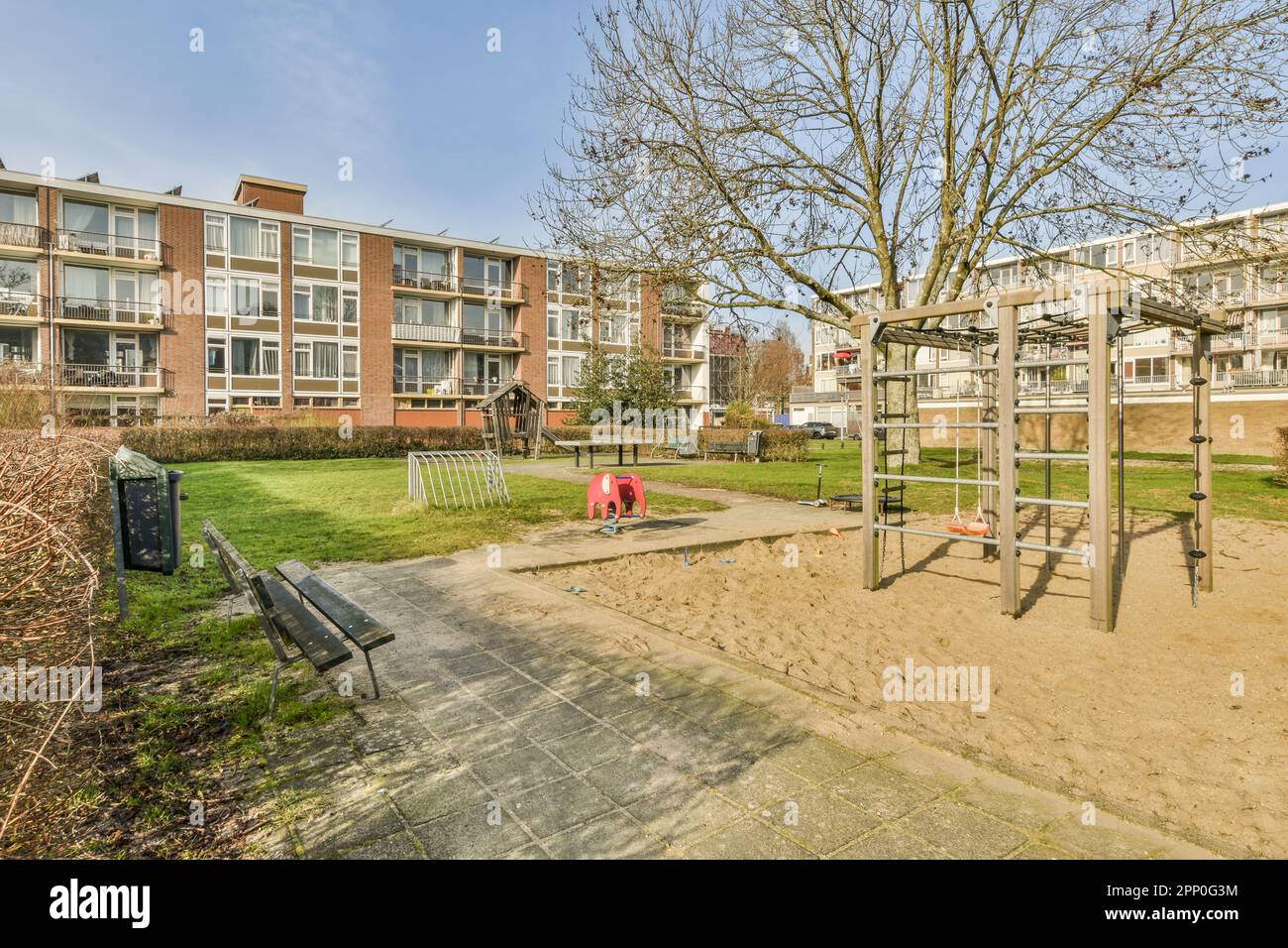 Ein leerer Spielplatz mitten in einem Wohngebiet mit Bäumen, Bänken und Kinderspielgeräten auf beiden Seiten Stockfoto