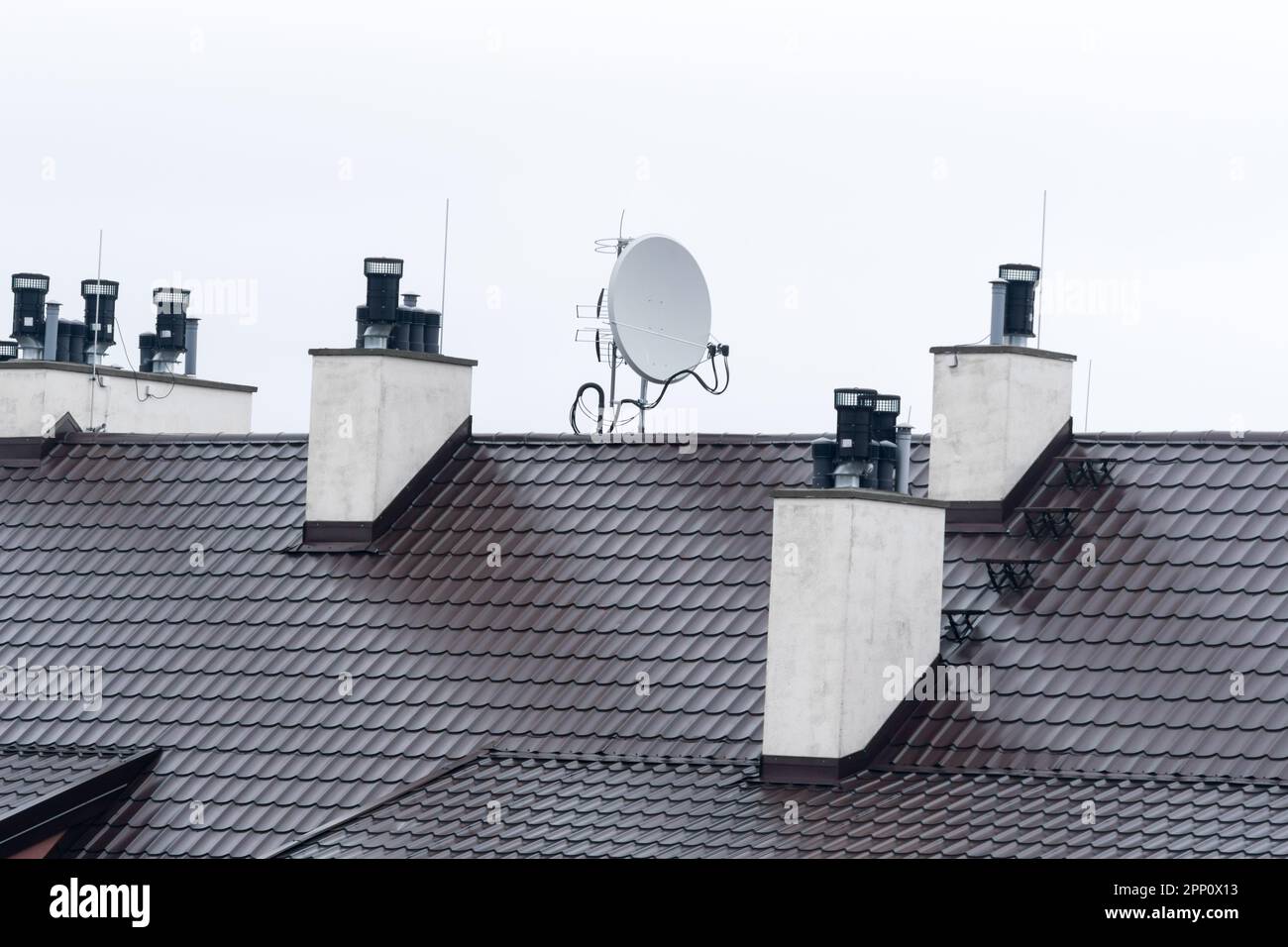 Blick auf das Dach des Gebäudes mit montierten Antennen und Lüftungsrohren am grauen Himmel Stockfoto