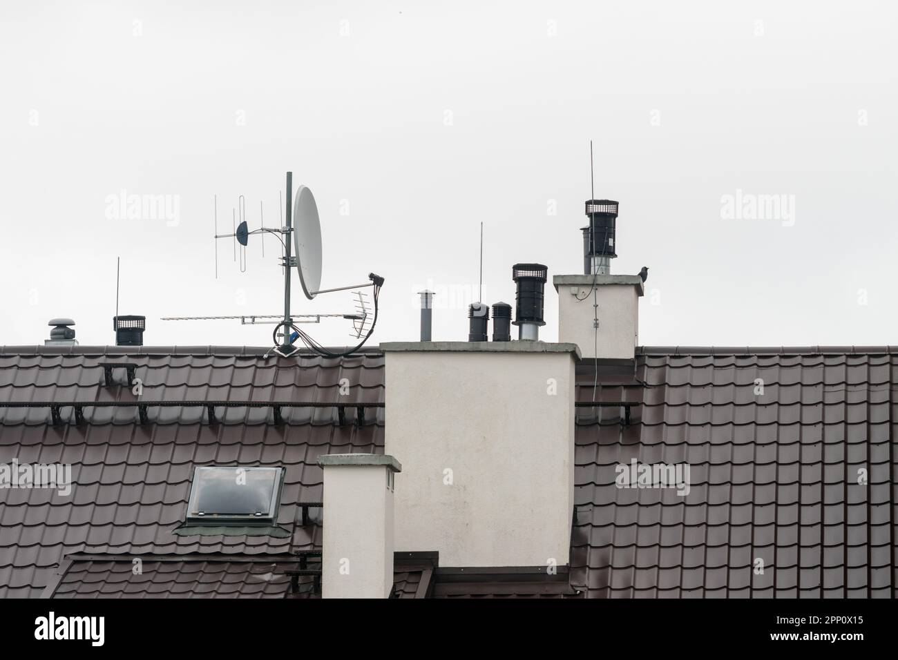 Blick auf das Dach des Gebäudes mit montierten Antennen und Lüftungsrohren am grauen Himmel Stockfoto