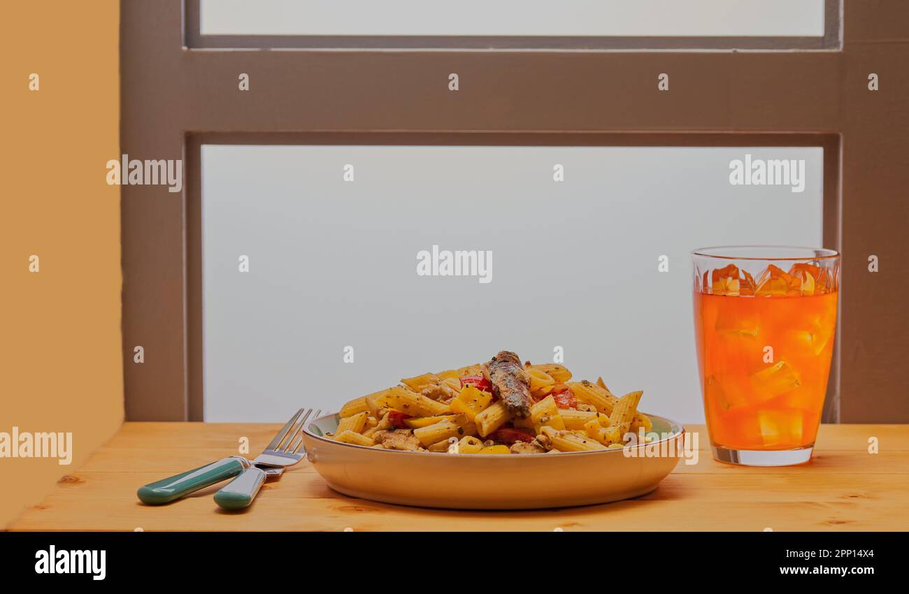 Sardinen- und Nudelgericht mit kaltem Getränk auf einem Tisch vor einem Fenster. Stockfoto