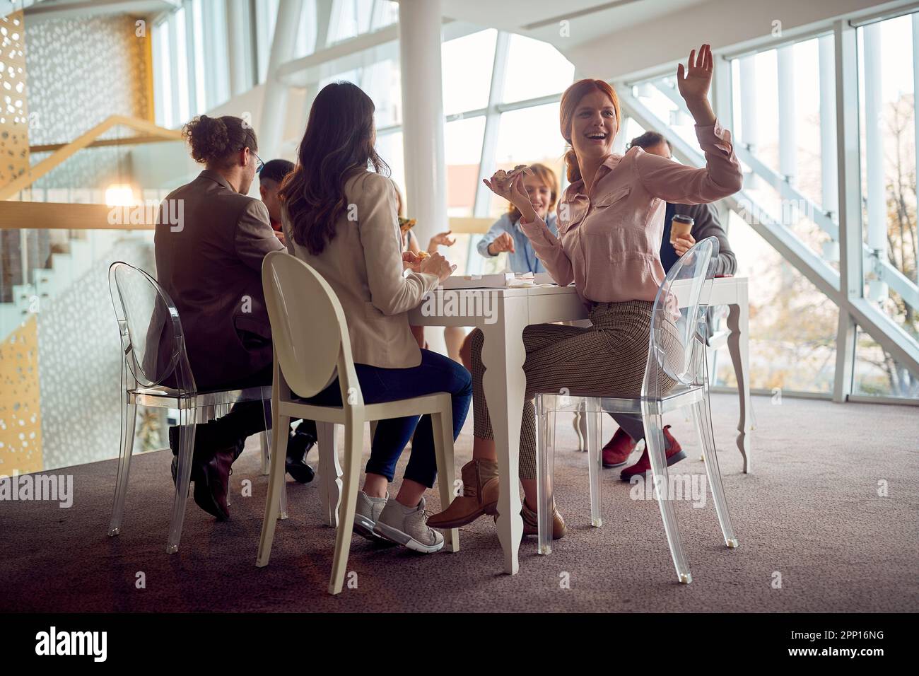 Junge Geschäftsleute sitzen während einer Mittagspause in einer freundlichen Atmosphäre im Firmengebäude am Tisch und amüsieren sich Stockfoto