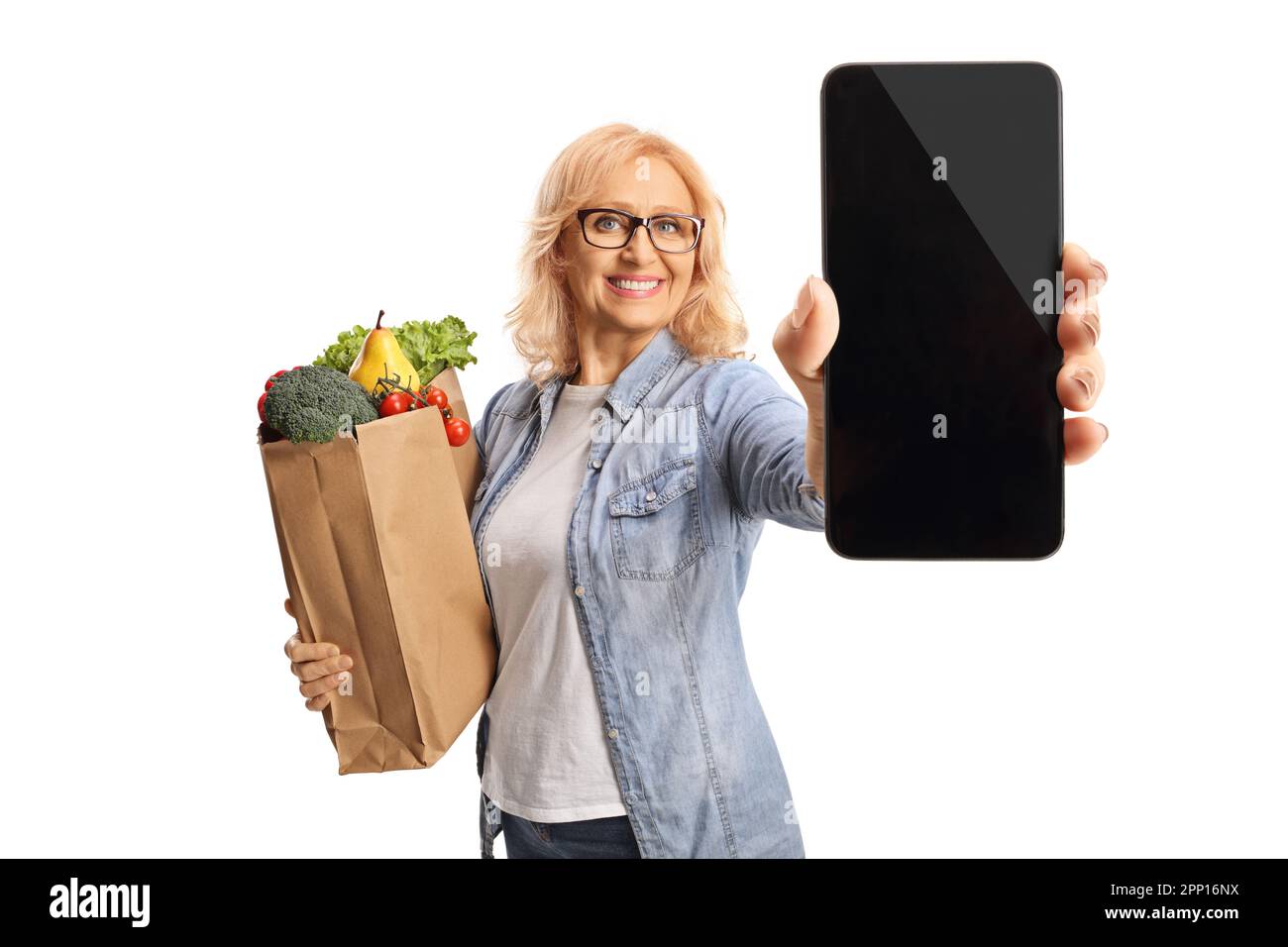 Reife Frau mit einer Einkaufstasche, die ein Smartphone isoliert auf weißem Hintergrund hält Stockfoto