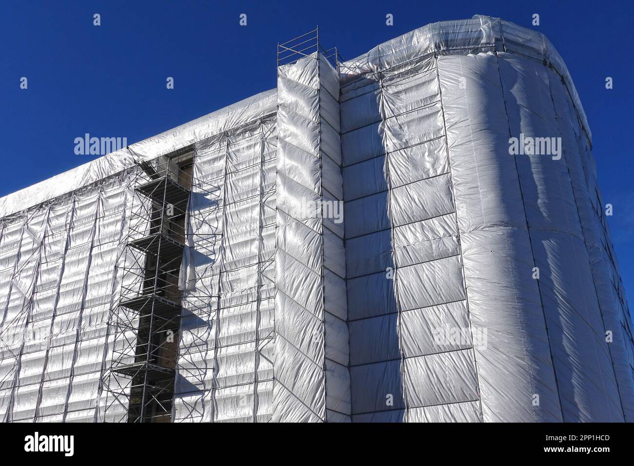 Gebäude-, Bau-, Renovierungs- oder Wartungsgelände mit Gerüsten und Schutzabdeckungen aus grauer Plane Stockfoto