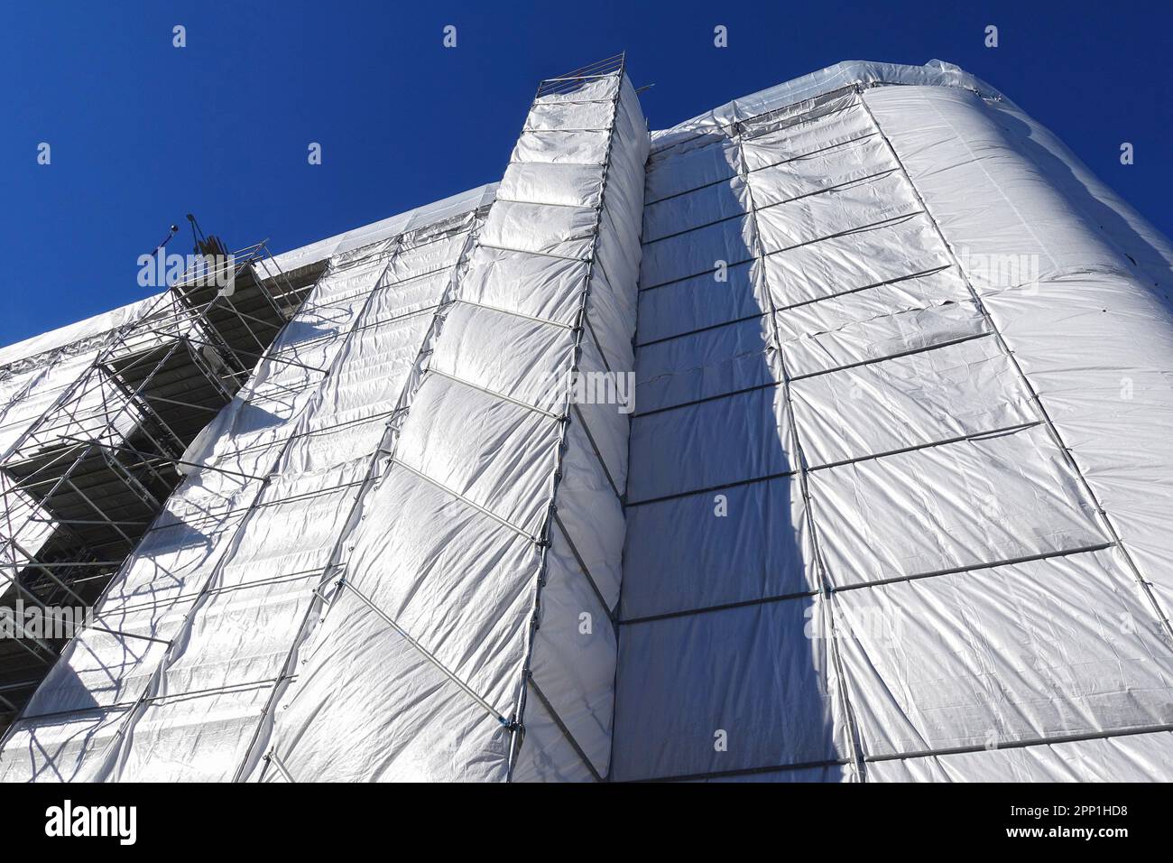 Gebäude-, Bau-, Renovierungs- oder Wartungsgelände mit Gerüsten und Schutzabdeckungen aus grauer Plane Stockfoto