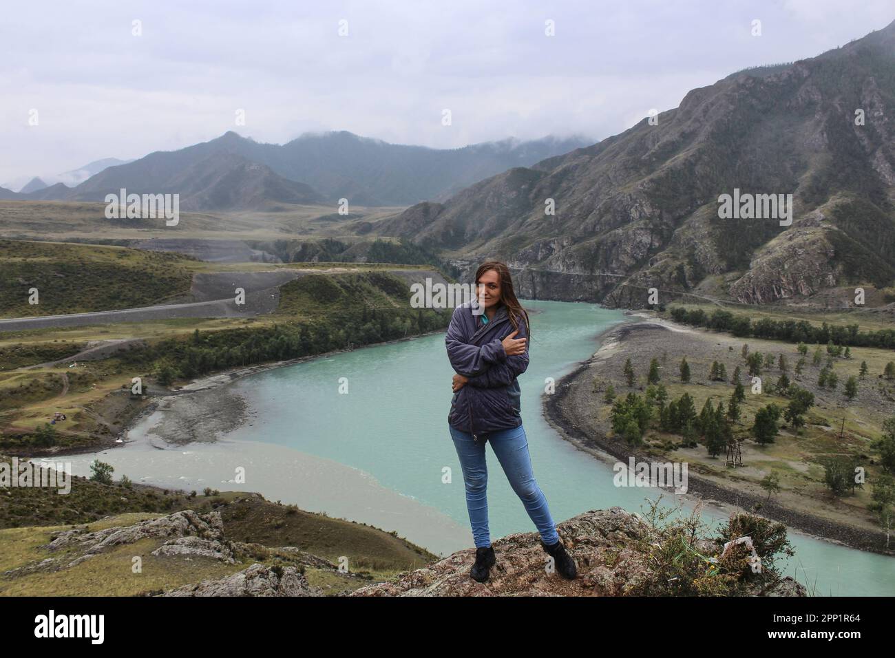 Junge Frau, die am Zusammenfluss zweier Flüsse verschiedener Farben, Chuya und Katun, steht. Berglandschaft, Altai Republik, Russland. Hohe Qual Stockfoto
