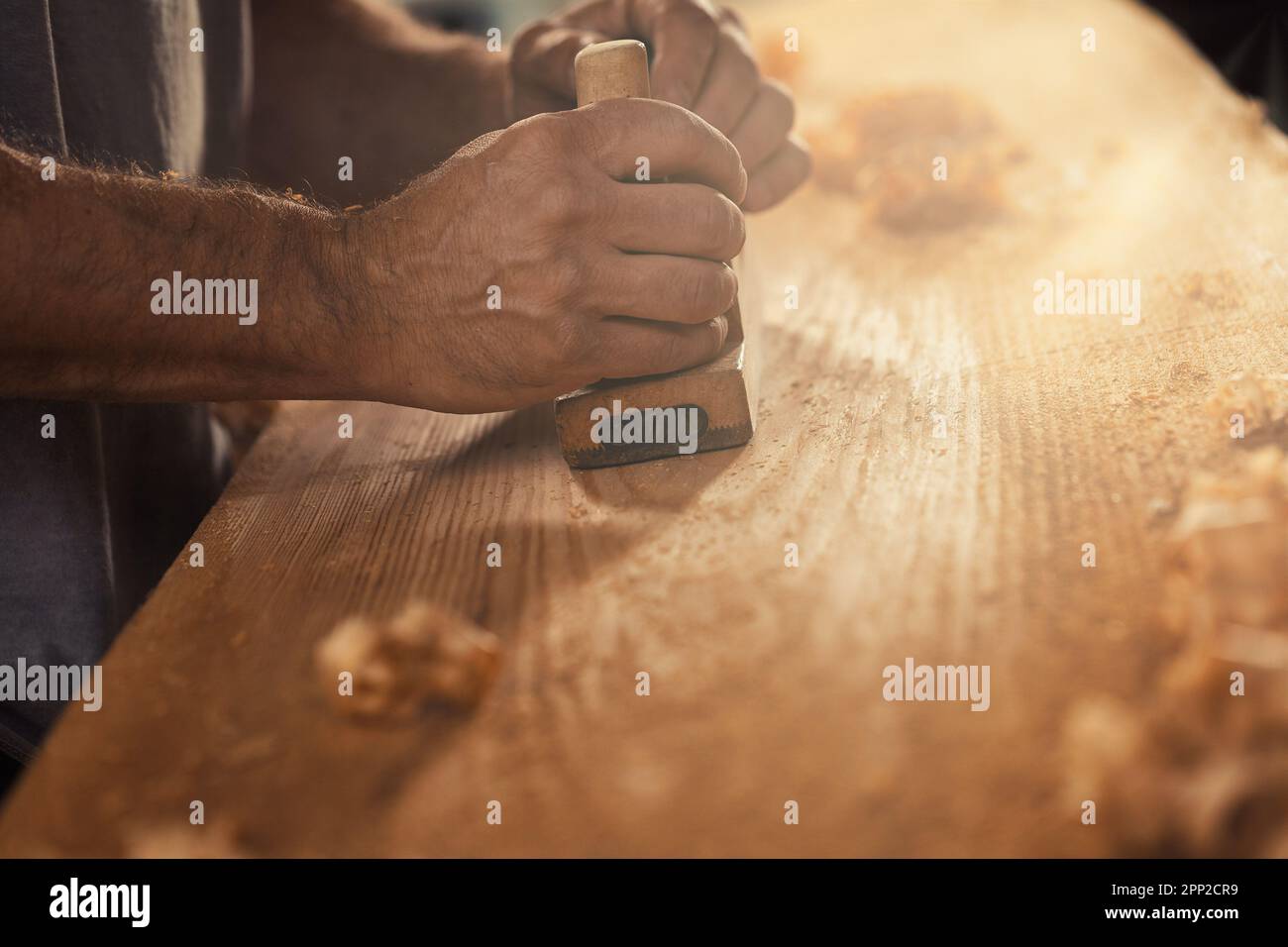 Der Holzhandwerker, ein robuster und starker Mann, der als Zimmermann bekannt ist, legt ein Brett auf traditionelle Weise und produziert Sägespäne, die aussehen Stockfoto