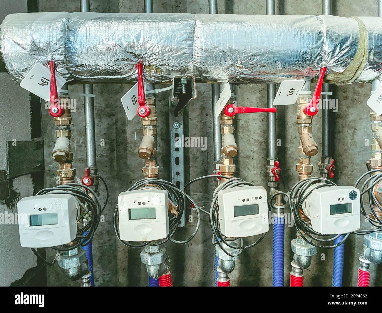 Messgeräte in einem Wohngebäude zur Messung der Wärmeenergie. Zähler mit roten Hähnen an einem Metallrohr in Folie. Bereitstellung von Ressourcen für residen Stockfoto