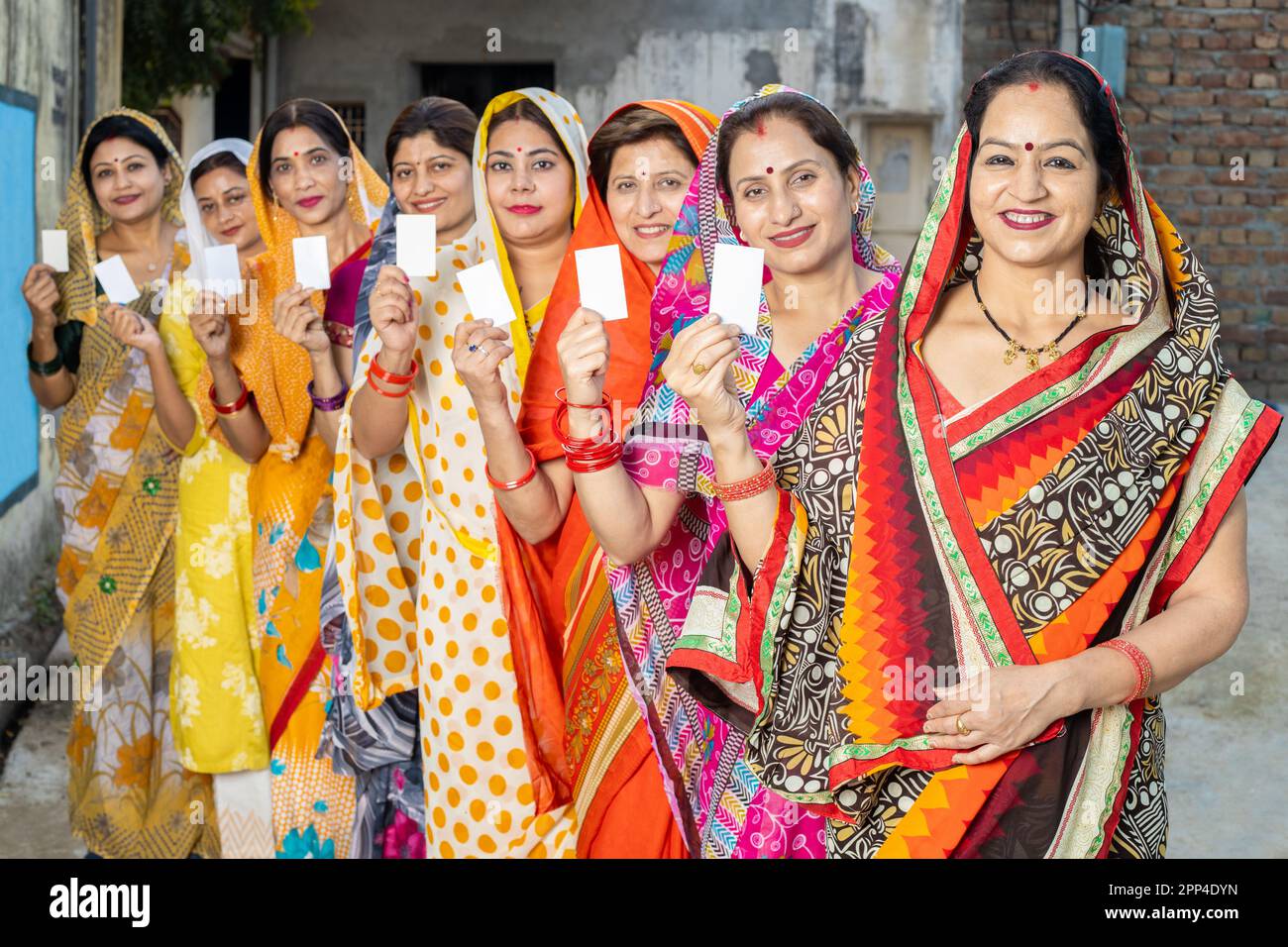 Eine Gruppe glücklicher, traditioneller indischer Frauen, die Sari tragen und in der Schlange stehen und einen leeren ausweis zeigen. Modell. Stockfoto