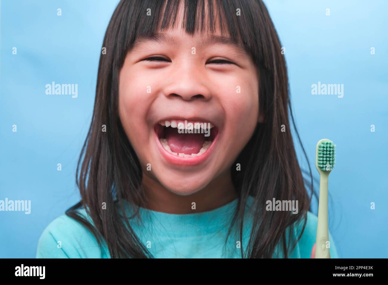 Lächelndes, süßes Mädchen, das eine Zahnbürste auf blauem Hintergrund hält. Süßes Kind, das Zähne putzt. Kind trainiert Mundhygiene, Zahnverfall früher Stockfoto