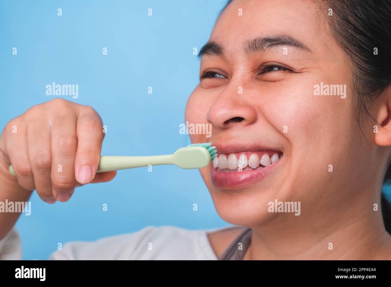 Glückliche Asiatin, die sich um ihre Zähne kümmert und eine Zahnbürste in der Hand hält. Junge Dame putzt sich die Zähne. Zahnpflege und Mundhygienekonzept. Stockfoto