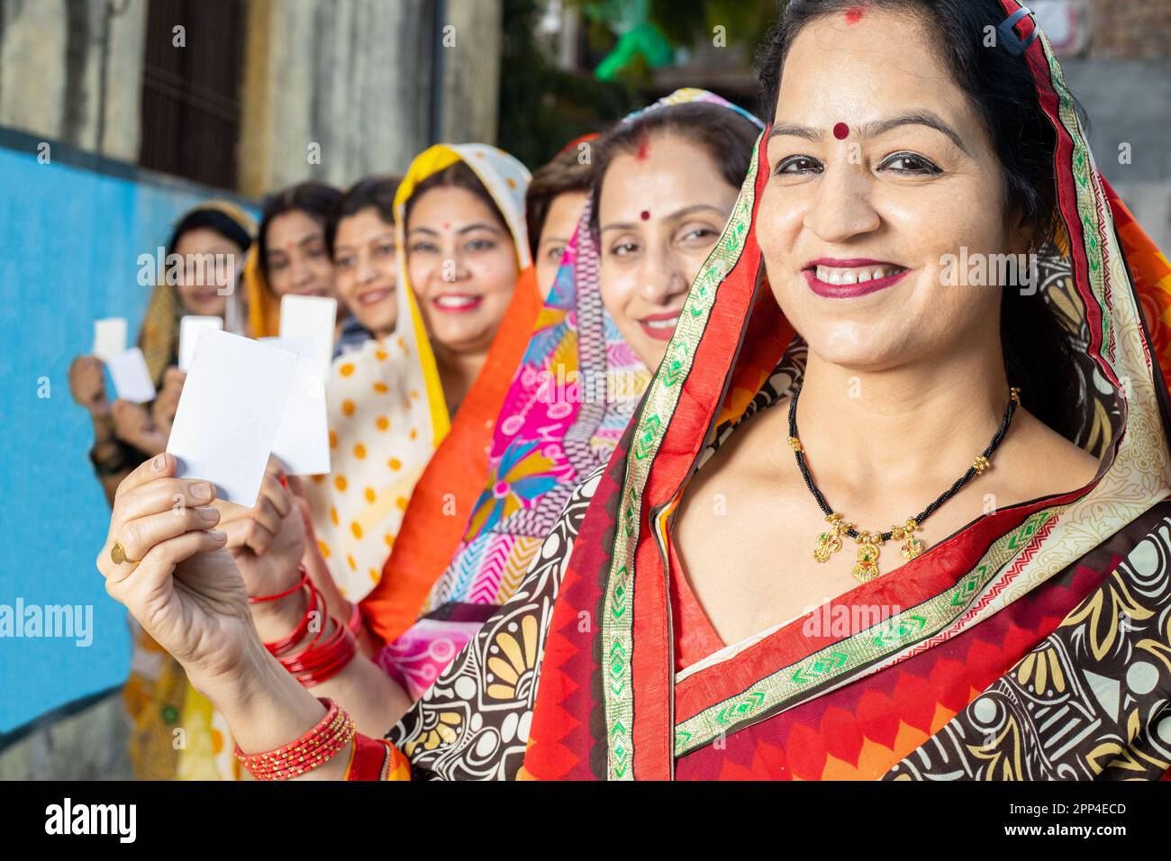 Eine Gruppe glücklicher, traditioneller indischer Frauen, die Sari tragen und in der Schlange stehen und einen leeren ausweis zeigen. Modell. Selektiver Fokus. Stockfoto