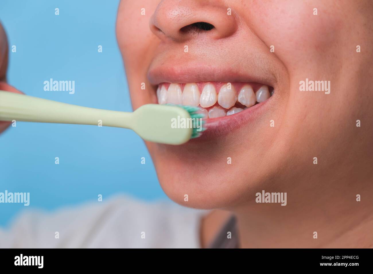 Glückliche Asiatin, die sich um ihre Zähne kümmert und eine Zahnbürste in der Hand hält. Junge Dame putzt sich die Zähne. Zahnpflege und Mundhygienekonzept. Stockfoto