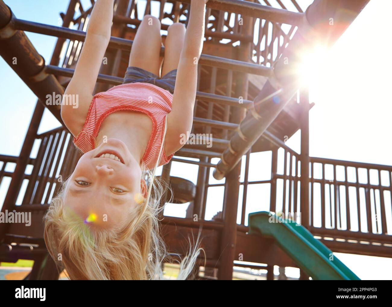 Der Spielplatz ist ihr Lieblingsort. Ein kleines Mädchen, das kopfüber auf dem Spielplatz an Affenbars hing. Stockfoto