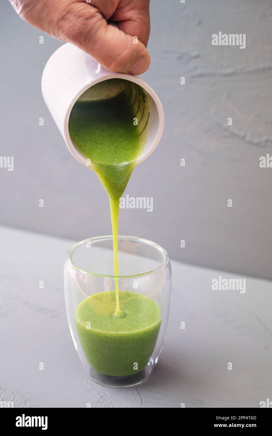 Grüner Smoothie oder Suppe aus wilden Kräutern und Gemüse wird in ein doppelwandiges Trinkglas vor grauem Hintergrund gegossen, gesundes Essen Conce Stockfoto