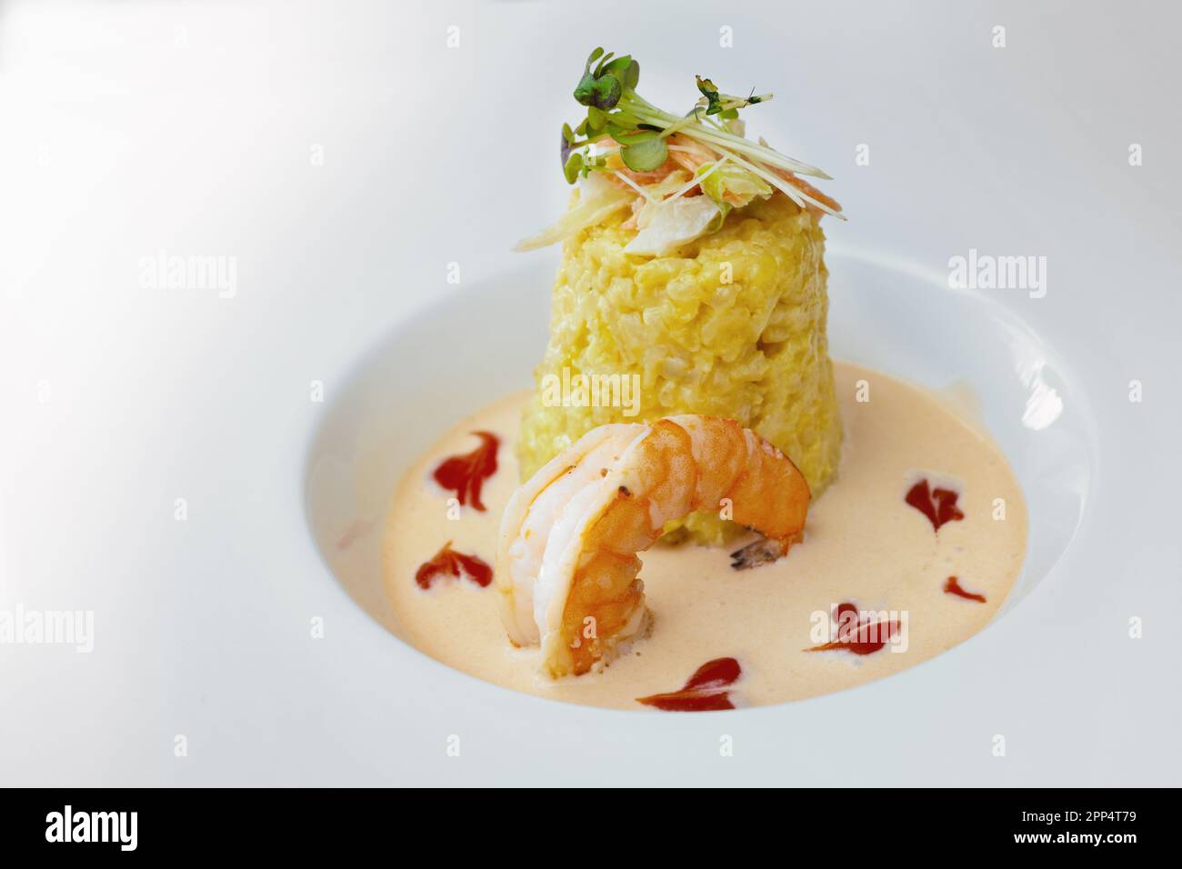 Gourmetgericht aus Safran-Risotto mit Gemüse- und Kräutergarnelen, einer großen Garnelen- und Krustentiersauce auf einem modernen weißen Teller, Kopierbereich, ausgewählt für Stockfoto